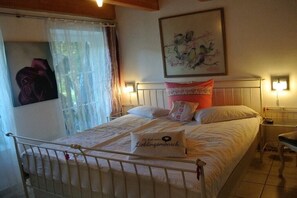 Een slaapkamer met een bed, een kussen met tekst, een schilderij aan de muur en een raam met gordijnen.