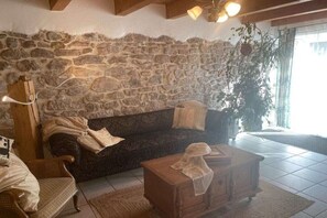 Een woonkamer met een stenen muur, een donkere bank, een houten stoel, een houten salontafel en een plant in een pot.