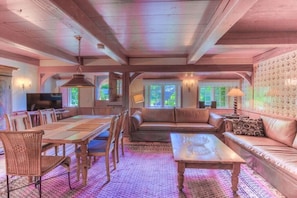 A cozy living room with a wooden ceiling, a sofa, a coffee table, and a dining area with chairs and a table. - Friesenhaus Sara (S3) (Wenningstedt)