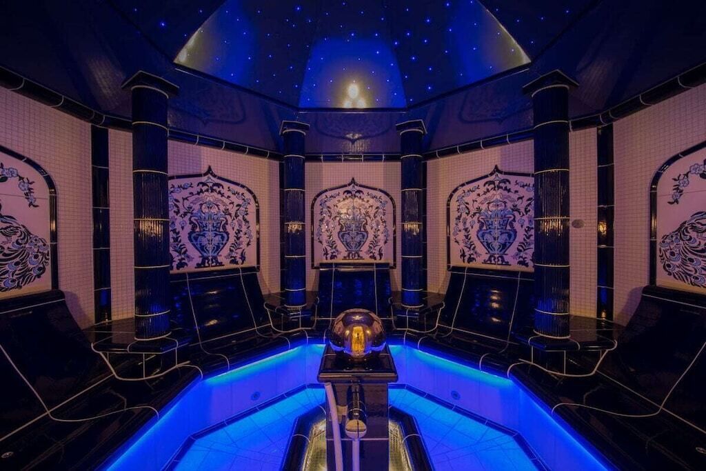 A luxurious spa room with a central hot tub, ornate wall designs, and a starry ceiling.