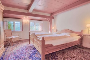 Une chambre à coucher avec un lit en bois, une chaise, une fenêtre avec des rideaux et un tapis à motifs.