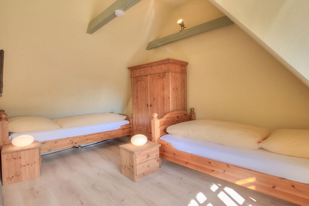 A bedroom with two wooden beds, a wooden wardrobe, and a small bedside table with a lamp.
