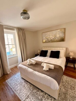 Une chambre d’hôtel avec un grand lit, une fenêtre avec des rideaux, un tableau au mur et un luminaire au plafond.