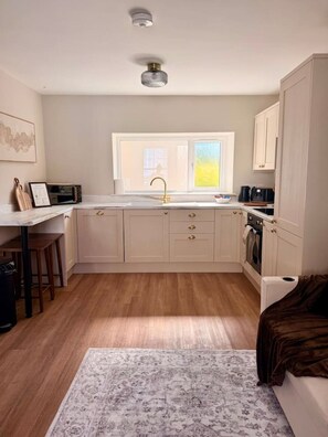 A compact kitchen with a window, wooden flooring, and a patterned rug. - 1 bed retreat in the heart of Tenby - Apartment 3 (Tenby)