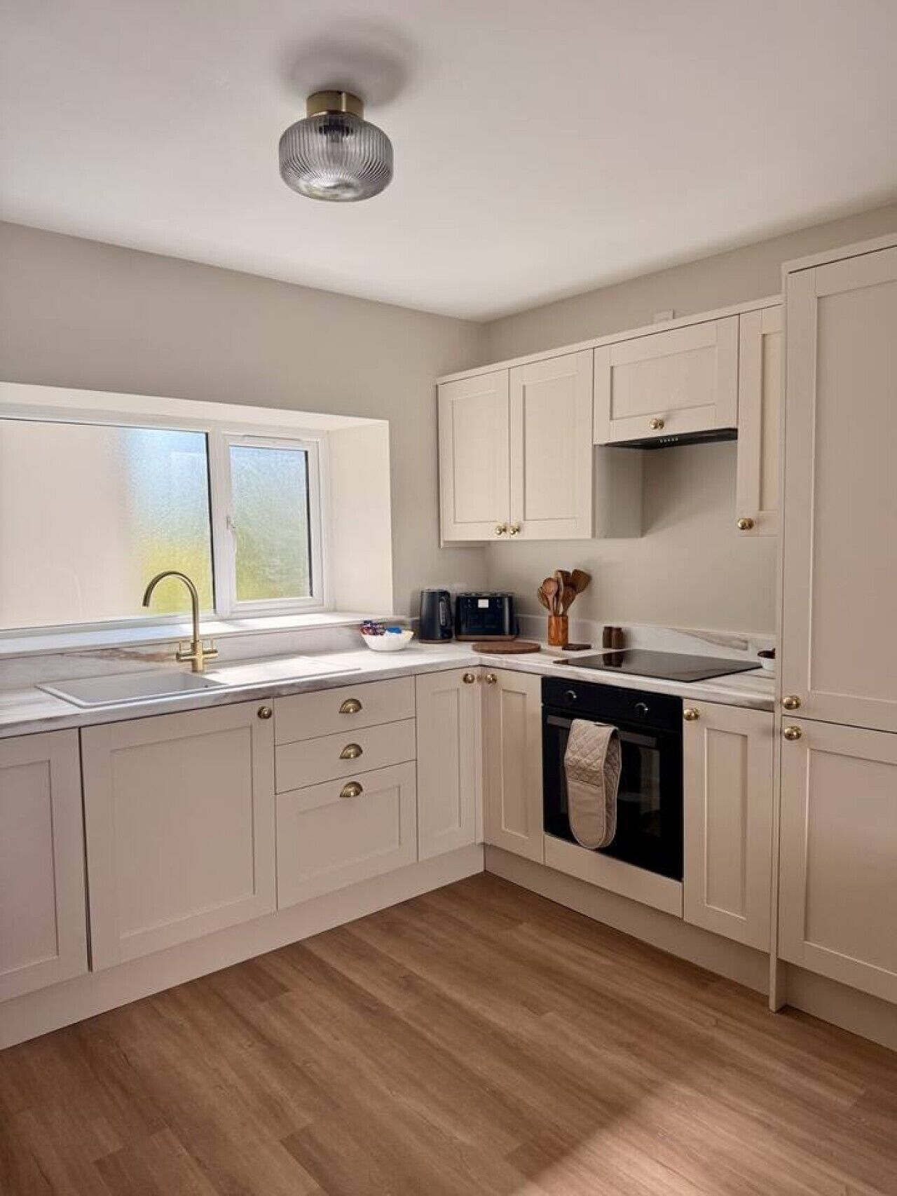 A kitchen with white cabinetry, a stainless steel sink, a black oven, and a window with frosted glass.