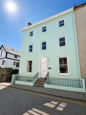 A two-story building with a white door, multiple windows, and a small set of stairs leading to the entrance. - 1 bed retreat in the heart of Tenby - Apartment 3 (Tenby)