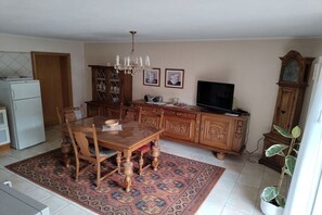 A dining area with a wooden table and chairs, a chandelier, a cabinet with decorative items, a television, and a clock. - Holiday apartment with 1 bedroom (Friesenhagen)