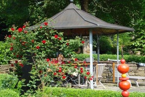 Ein Gazebo mit Metalldach, umgeben von üppigem Grün und roten Blüten.