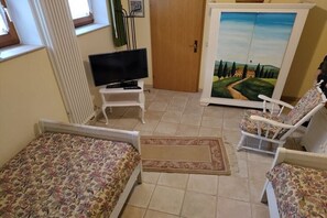 Ein Zimmer mit einem Bett, einem Fernseher auf einem kleinen Tisch, einem Schrank mit einem Landschaftsbild und zwei Stühlen.