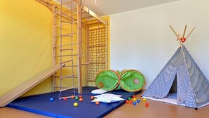 Espaço de brincadeiras com um escorrega, tapete macio, um tipi e bolas coloridas.
