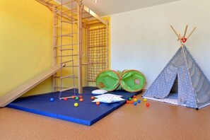Ein Spielbereich mit einer Kletterleiter, einer weichen Krabbeldecke, einem Zelt und bunten Bällen.