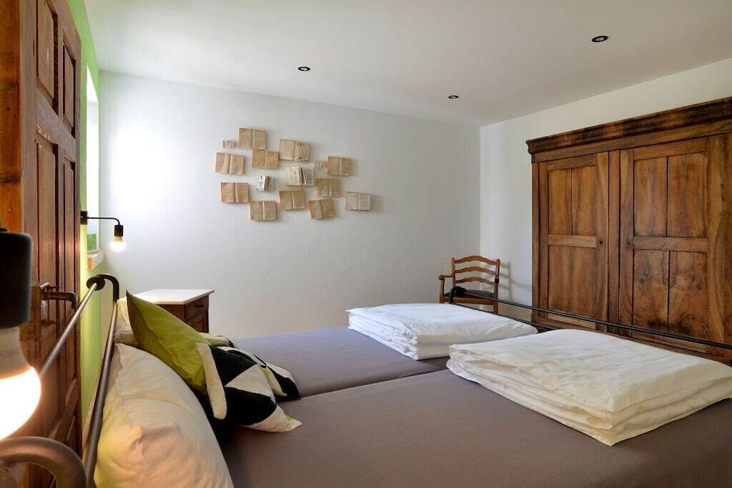 A room with two beds, a wooden wardrobe, and a wall-mounted light fixture.