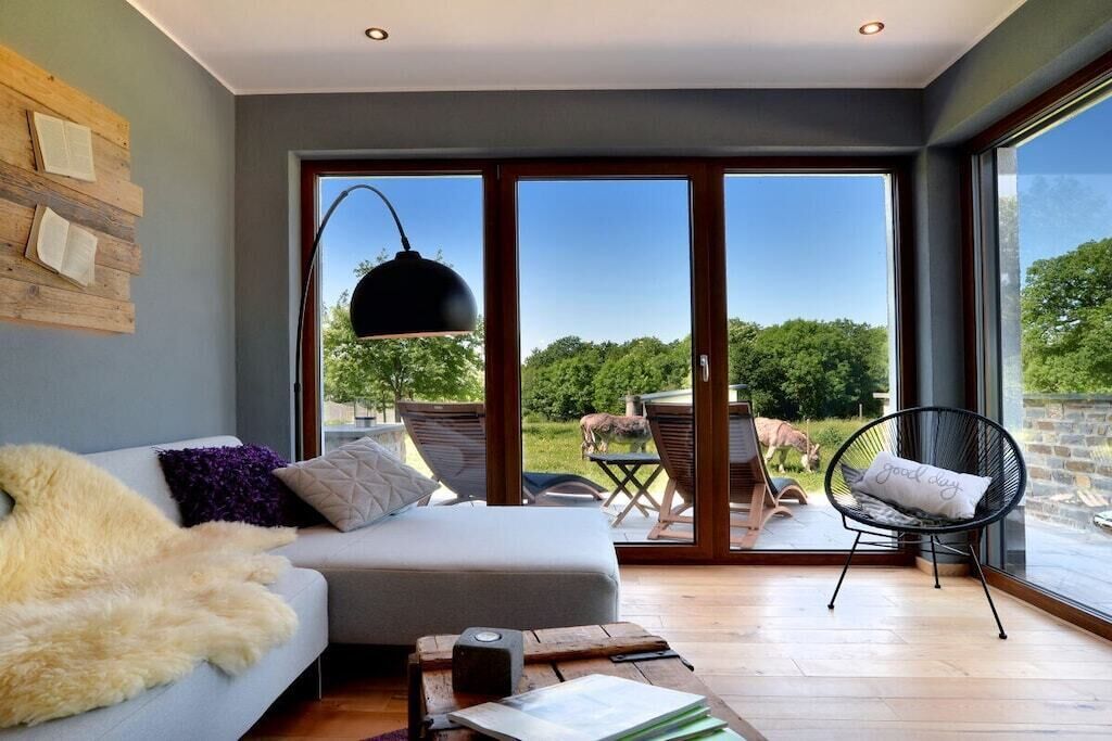 A modern living room with a sofa, a chair, a table, and a large window with a view of greenery.