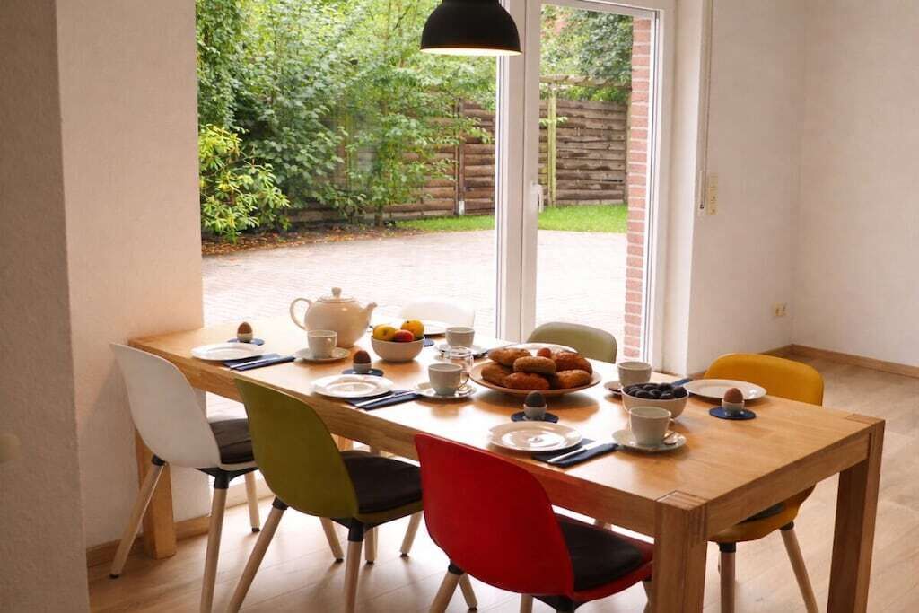 Un coin repas avec une table en bois, quatre chaises et une vue sur un jardin, visible à travers une porte vitrée.