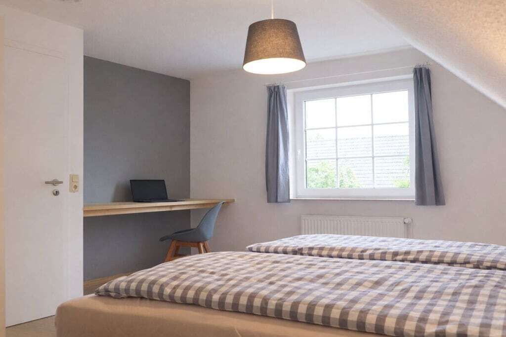 A bedroom with two beds, a desk, a chair, and a window with curtains.