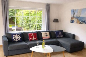 Ein Wohnzimmer mit einem grauen Sofa, einem runden Tisch und einem Fenster mit Vorhängen.