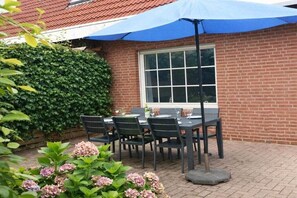 Eine Terrasse im Freien mit einer Ziegelwand, einem Fenster und einem Tisch mit Stühlen.