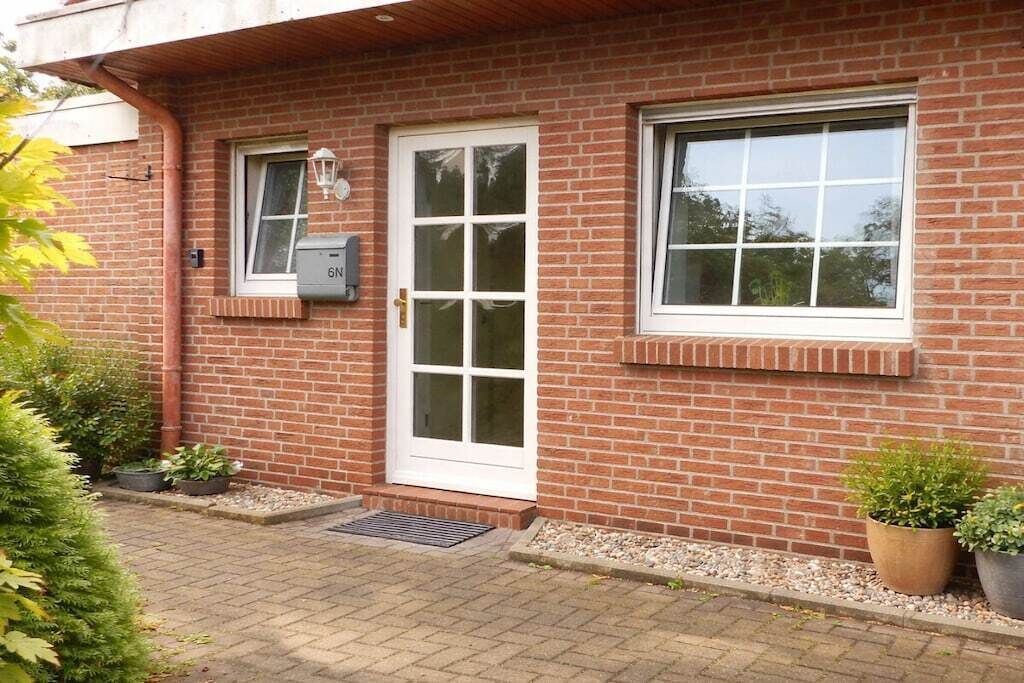 Un bâtiment en briques avec une porte et des fenêtres blanches, une boîte aux lettres et des plantes en pot.