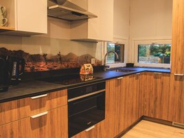 Eine moderne Küche mit Holzschränken, einem schwarzen Geschirrspüler und einem Fenster mit Blick ins Grüne.
