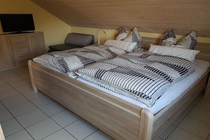 Ein Schlafzimmer mit einem hölzernen Bett, einem Fernseher auf einem Schrank und einem Sessel.