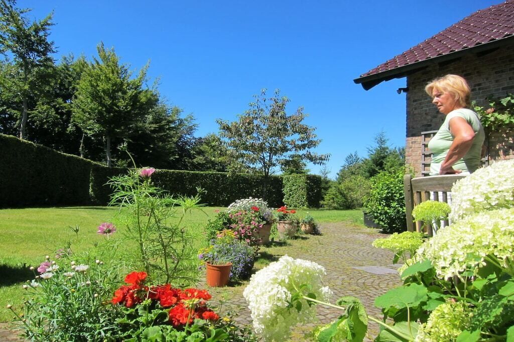 A garden with various plants and flowers, a brick building, and a clear blue sky.