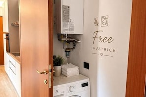 A bathroom with a white wall, a door with a brass handle, a white washing machine, and a towel stack. - Venice Easy Stay | New Apartment with Parking (Mestre)