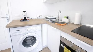 Een kleine keuken met een wasmachine, koffiezetapparaat, spoelbak en kookplaat.