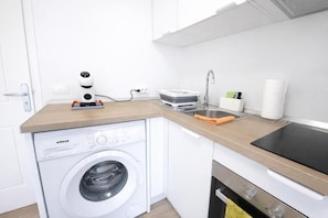 Una cocina compacta equipada con lavadora, cafetera, pileta y estufa.