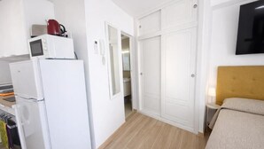 Een compacte kamer met een bed, een klein nachtkastje, een aan de muur bevestigde televisie en een kitchenette met een magnetron, broodrooster en koelkast.