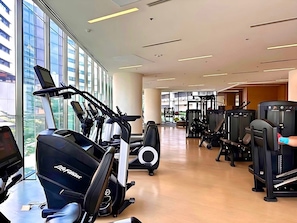 Een fitnessruimte met cardioapparatuur, gewichten en een groot raam dat natuurlijk licht binnenlaat.