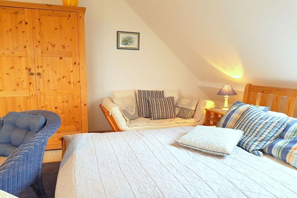 A bedroom with a bed, a chair, a wooden wardrobe, and a bedside table with a lamp.