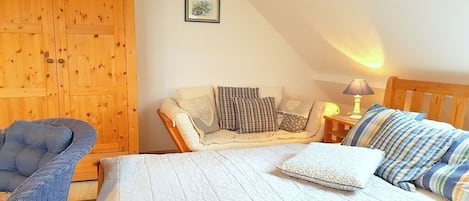 A bedroom with a bed, a chair, a wooden wardrobe, and a bedside table with a lamp.