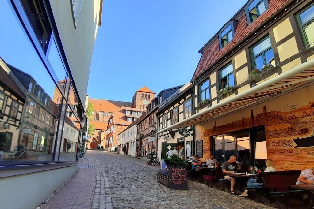Una calle empedrada con edificios tradicionales, mesas al aire libre y un cielo despejado.