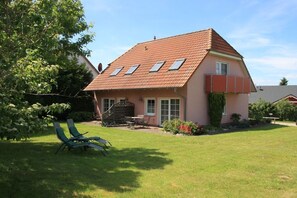 A house with a sloped roof, a front porch, and a garden with a lawn and two chairs. - Holiday apartment with 0 bedrooms (Röbel OT Gotthun)