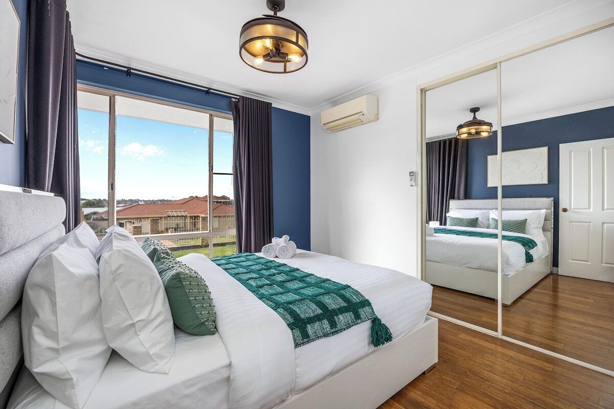 A hotel room with a large bed, a mirror, a view through the window, and a ceiling fan.