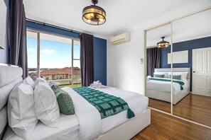 A hotel room with a large bed, a mirror, a view through the window, and a ceiling fan. - The Beach House|4BR+Spa+Jacuzzi|2 Min Coogee Beach (Coogee)