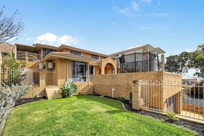 A two-story residential building with a brick facade, a covered patio, and a well-maintained lawn.