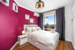 A bedroom with a large bed, bedside tables, a nightstand, a ceiling light fixture, and a window with curtains.