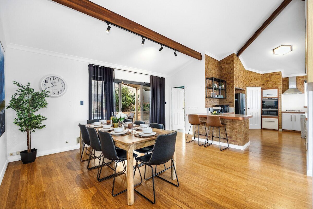 A modern kitchen with a brick accent wall, wooden flooring, and a dining area with a wooden table and chairs.