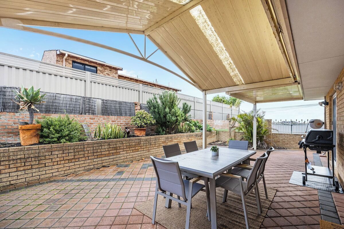 A covered patio with a table and chairs, a grill, and potted plants.