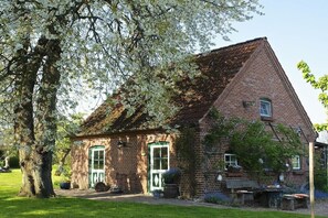 Un bâtiment en briques avec un toit à deux versants, une porte verte et un petit porche doté de sièges extérieurs.