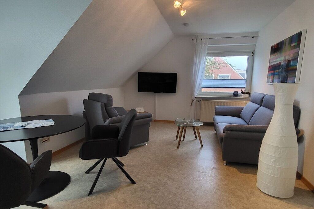 Een moderne woonkamer met een flatscreen televisie aan de muur, een bank, een salontafel en een grote witte vaas.