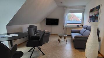Een moderne woonkamer met een flatscreen televisie aan de muur, een bank, een salontafel en een grote witte vaas.