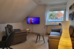 A living room with a television, sofas, a coffee table, and a window with curtains. - Holiday apartment with 1 bedroom (Neuharlingersiel)