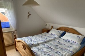 Ein Schlafzimmer mit einem hölzernen Bett, einem Nachttisch, einer Lampe und Blick durch ein Fenster.