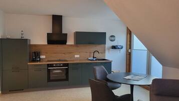Een moderne keuken met een ingebouwde oven, een koffiezetapparaat en een spoelbak. Er is een eethoek met een tafel en stoelen.