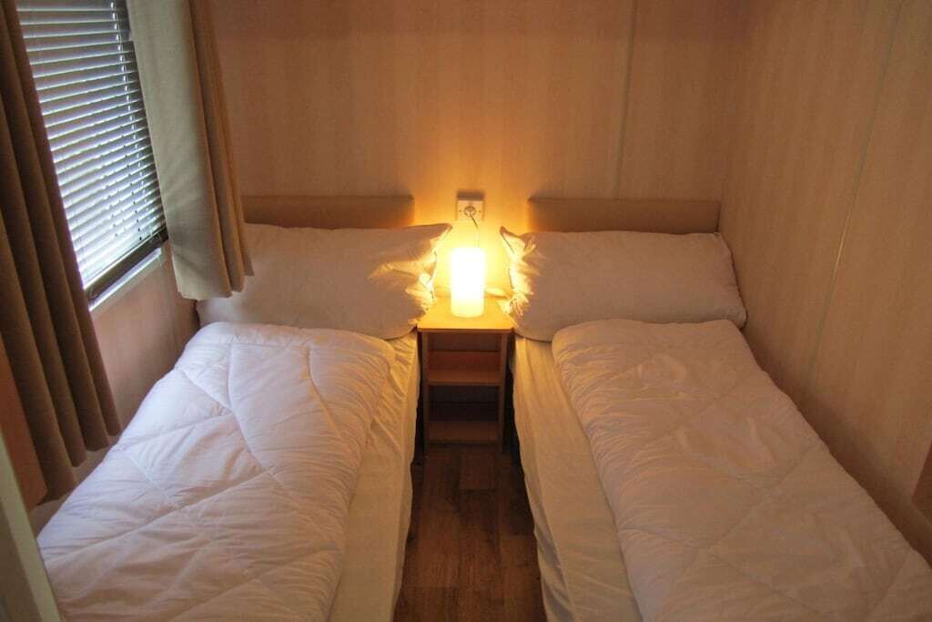 A small, cozy room with two beds, a nightstand, and a window with curtains.