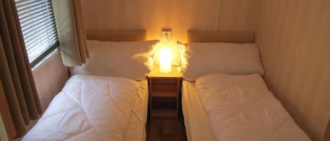 Una habitación pequeña y acogedora con dos camas, una mesita de noche y una ventana con cortinas.
