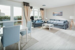 A modern living room with a sofa, coffee table, and a dining area with a table and chairs. - Holiday apartment in Juist with swimming pool (Juist)