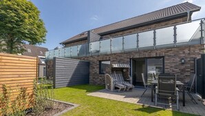 Een modern huis met een glazen balkon, een terras met tuinmeubilair en een verzorgd gazon.